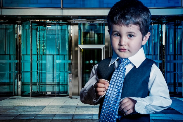 Enfant professionnel habillé homme d'affaires avec les mains dans sa cravate et gratte-ciel en arrière-plan