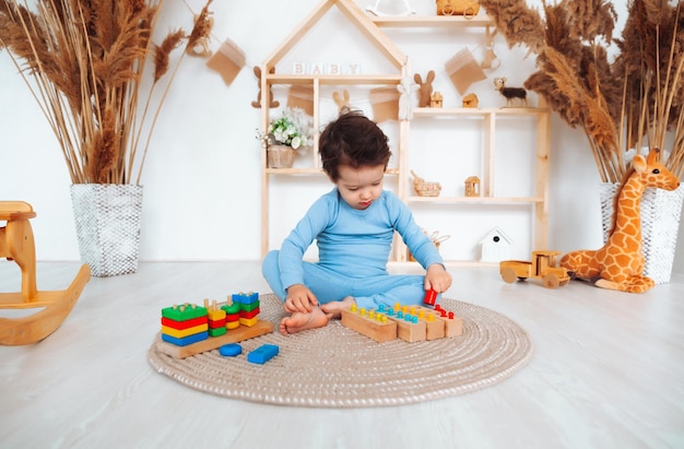 Un enfant en pyjama est assis par terre dans sa chambre et joue avec un kit de construction en bois jouets naturels pour enfants le garçon joue dans sa chambre