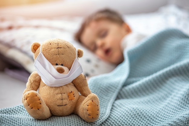 Enfant en quarantaine à domicile sur le lit, dormant, avec un masque médical sur son ours en peluche malade, pour se protéger contre les virus pendant le coronavirus