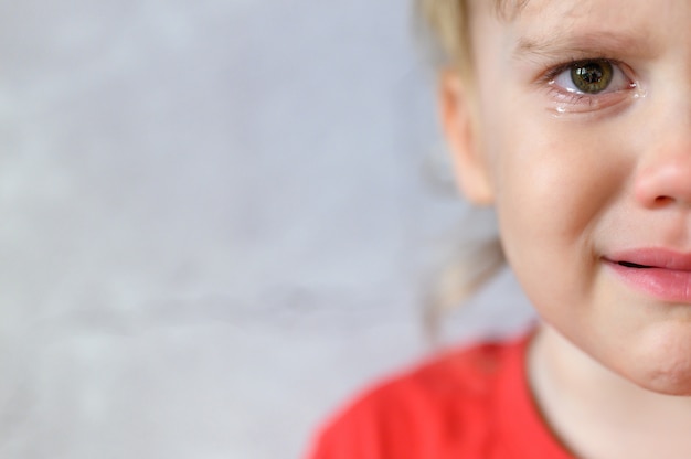 Enfant qui pleure. le visage d'un mignon petit garçon de quatre ans bouleversé en larmes. le chagrin des enfants. fond de mur en béton gris. espace pour le texte