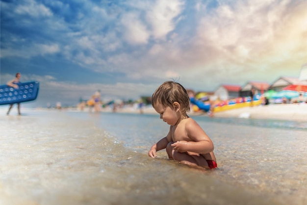 Un enfant ramasse des coquillages et des cailloux dans la mer sur un fond sablonneux sous le soleil d'été en vacances