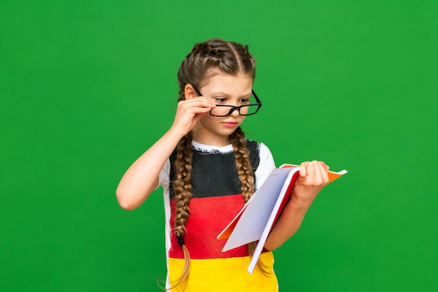 Un enfant réfléchi avec un drapeau allemand et un cahier dans ses mains sur un fond vert isolé Cours d'allemand pour écoliers