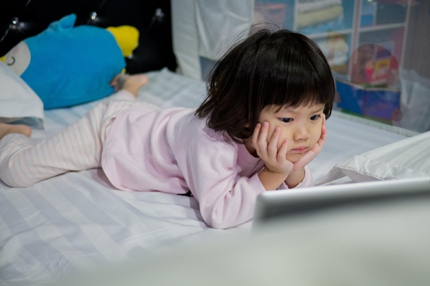 Enfant regardant une tablette sur le lit dessin animé enfant accro