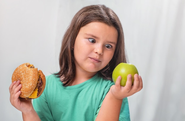 Un enfant regarde une pomme avec surprise après avoir croqué dans un hamburger