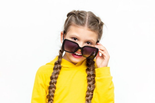 L'enfant regarde sous des lunettes de soleil Une belle petite fille dans un costume d'été jaune sur un fond blanc isolé