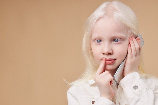 Enfant rêveur réfléchi atteint du syndrome d'albinisme parlant au téléphone