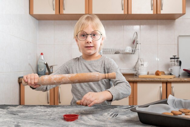 Enfant avec rouleau à pâtisserie dans ses mains roule la pâte à biscuits