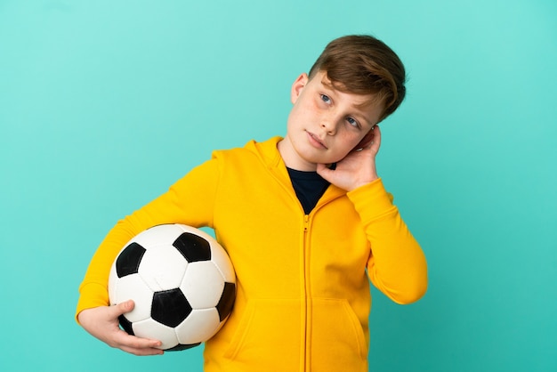 Enfant rousse jouant au football isolé sur fond bleu ayant des doutes