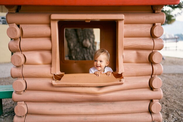 L'enfant s'assied dans une maison de jouet près de la fenêtre sur le terrain de jeu