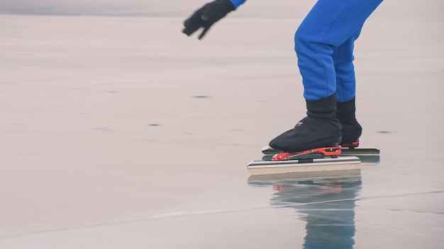 L'enfant s'entraîne au patinage de vitesse sur glace. Les jambes en patins se bouchent. La petite fille patine en hiver dans des lunettes de sport sportswear. Ralenti extérieur.