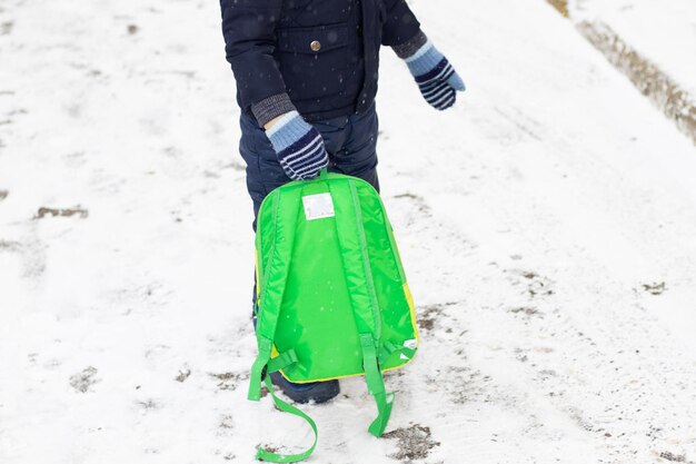 enfant avec sac à dos vert va à la maternelle hiver neige à l'extérieur des vêtements chauds