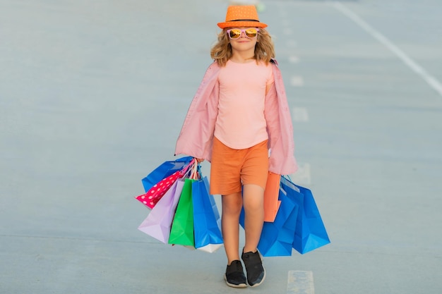 Enfant avec des sacs d'achat marchant dans la rue Enfant avec beaucoup de sacs de shopping en plein air petit garçon mignon en fa