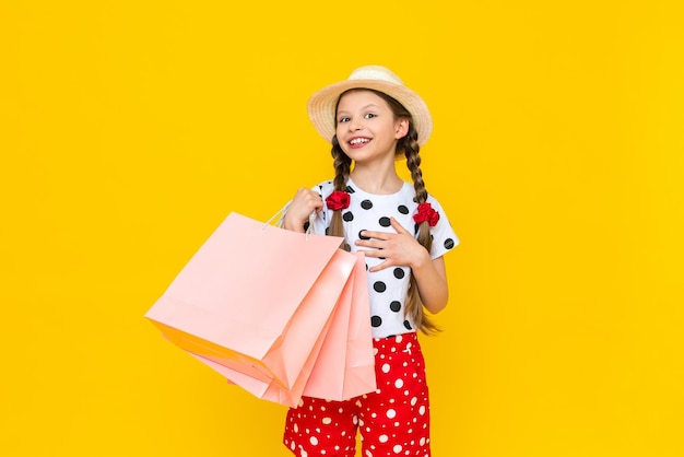 Un enfant avec des sacs en papier du magasin Achats d'été pour les enfants Une belle petite fille dans un chapeau sourit largement Fond isolé jaune