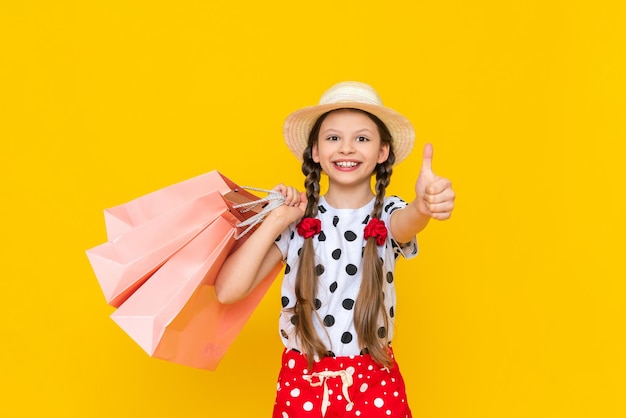 Un enfant avec des sacs en papier du magasin Achats d'été pour les enfants Une belle petite fille dans un chapeau sourit largement Fond isolé jaune