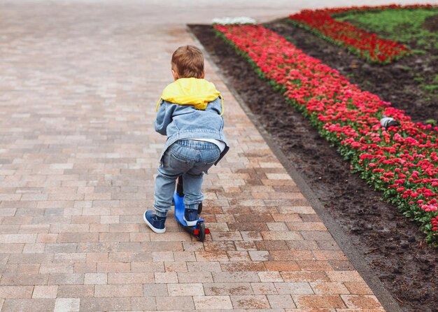 Enfant sur un scooter dans le parc Un petit garçon monte un scooter par une journée ensoleillée Sports actifs pour les enfants d'âge préscolaire