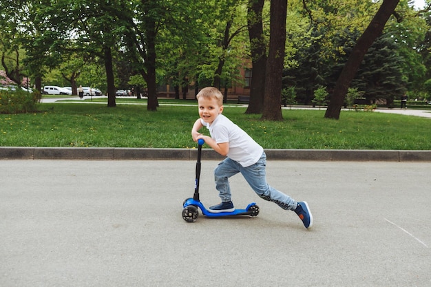 Enfant sur un scooter dans le parc Un petit garçon monte un scooter par une journée ensoleillée Sports actifs pour les enfants d'âge préscolaire