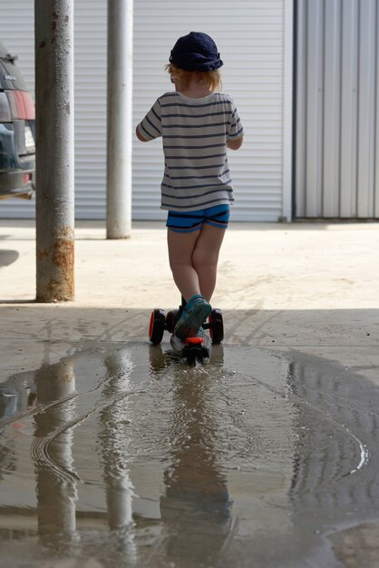 Un enfant en scooter traverse une flaque d'eau