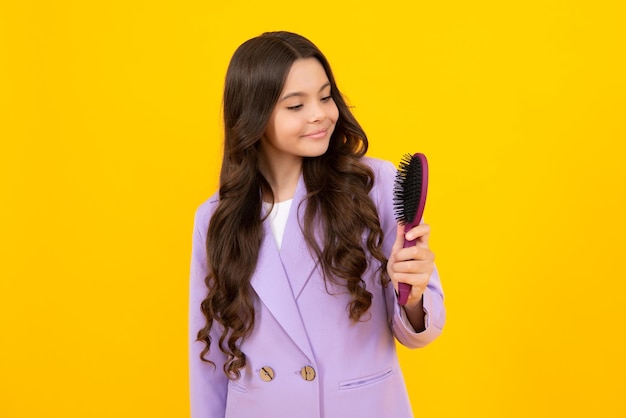 Enfant se brosser les cheveux avec un grand peigne sur fond de studio isolé jaune