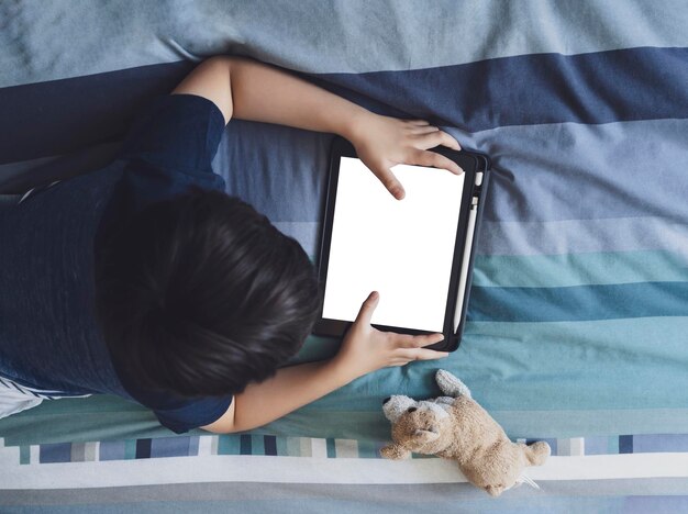 Enfant se détendant sur le lit à la maison enfant regardant des dessins animés sur une tablette numérique
