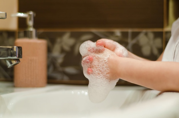 L'enfant se lave les mains avec du savon antibactérien avec de la mousse. hygiène quotidienne de l'enfant. prévention des maladies virales et bactériennes