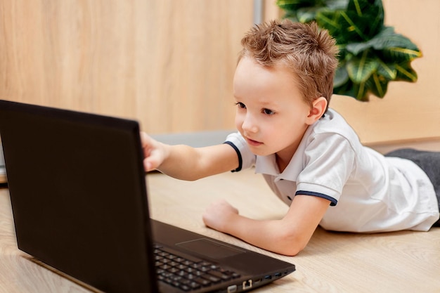 L'enfant se trouve sur le sol regarde l'ordinateur et pointe avec sa main vers le moniteur