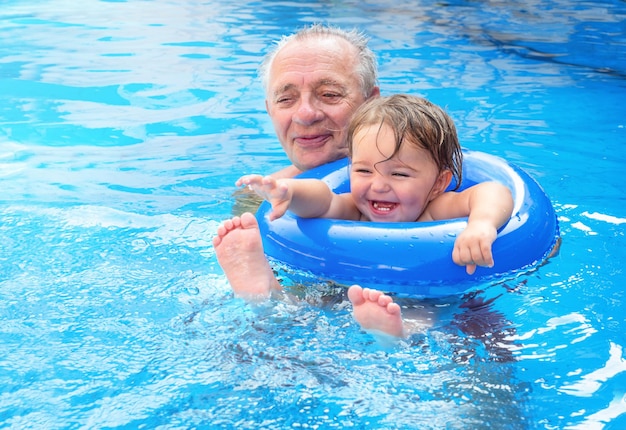 Un enfant avec un senior nage dans un cercle gonflable dans la piscine