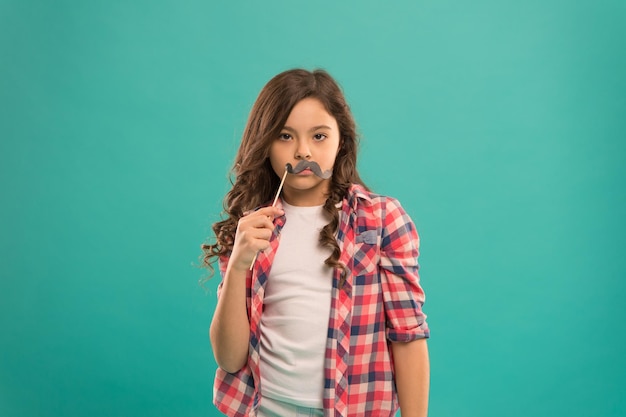 Enfant sérieux avec une drôle de moustache de fête. écolière prête à s'amuser. enfance heureuse. l'enfant essaie de créer une humeur positive. l'air drôle avec la moustache. petite fille préfet de la mode décontractée.