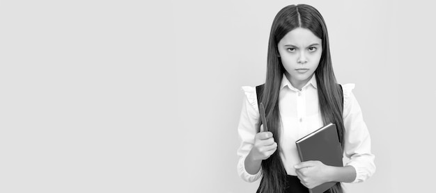 Enfant sérieux froncer les sourcils tenir livre scolaire et stylo fond jaune Portrait d'écolière étudiant studio bannière en-tête écolier face copyspace