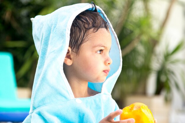 Enfant avec une serviette à capuche face à l'avant tout en mangeant des fruits