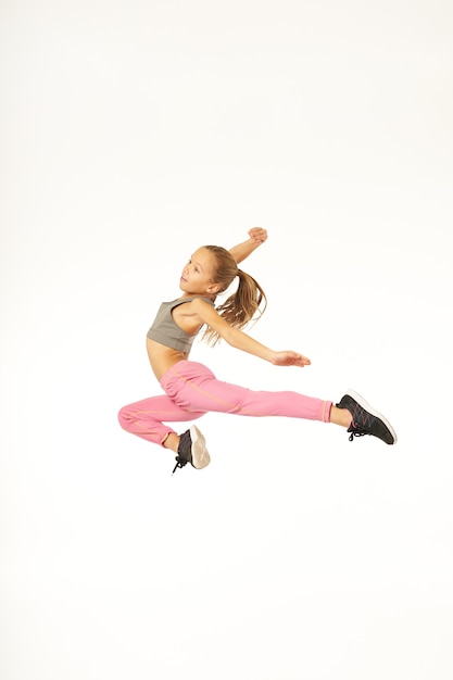 Enfant de sexe féminin mignon faisant un tour de gymnastique et souriant tout en sautant en studio. Isolé sur fond blanc