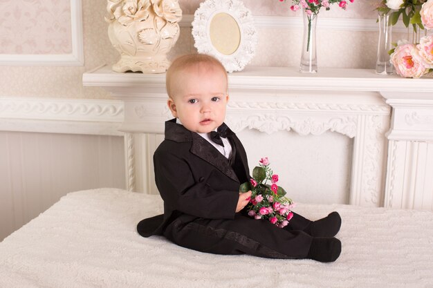 Enfant en smoking assis sur le lit à côté de la cheminée avec des fleurs dans leurs mains.