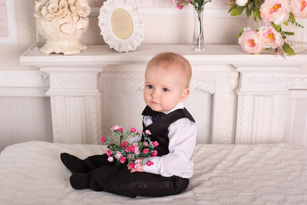 Enfant en smoking assis sur le lit à côté de la cheminée avec des fleurs dans leurs mains.