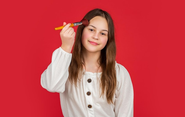 Un enfant souriant applique de la poudre sur le visage avec un pinceau de maquillage