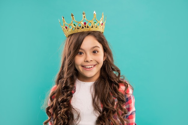 Enfant souriant aux cheveux bouclés dans la couronne de la reine sur fond bleu, béat.