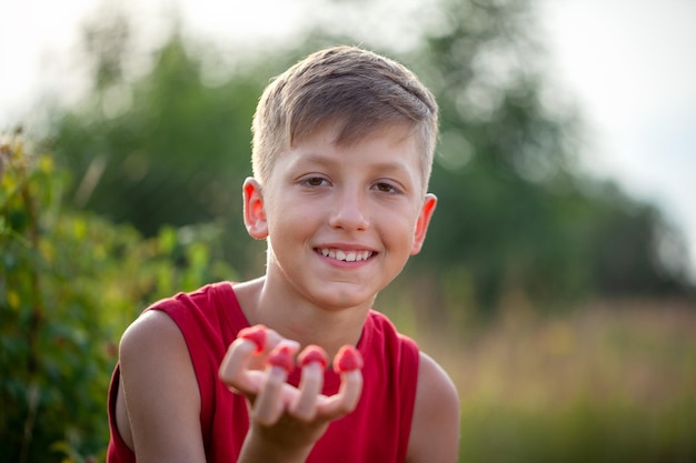 Enfant souriant cueillant et mangeant des framboises mûres fraîches dans le jardin d'été ou l'arrière-cour. Récolte d'été.