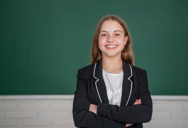 Enfant souriant debout sur fond de tableau noir dans la salle de classe à l'école