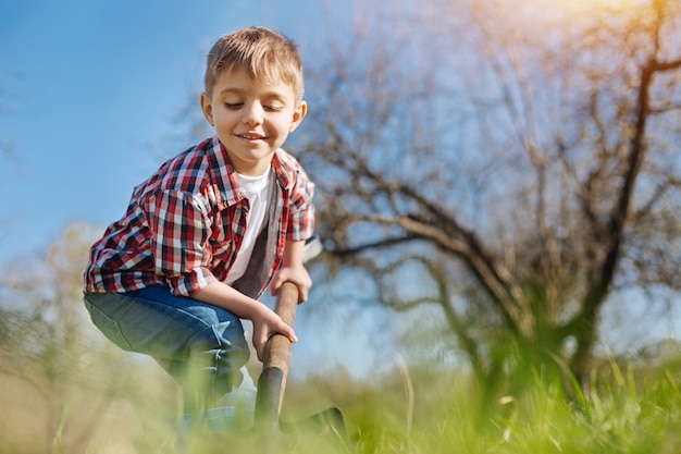 Un enfant souriant gai ramasser le sol avec une pelle dans un jardin familial