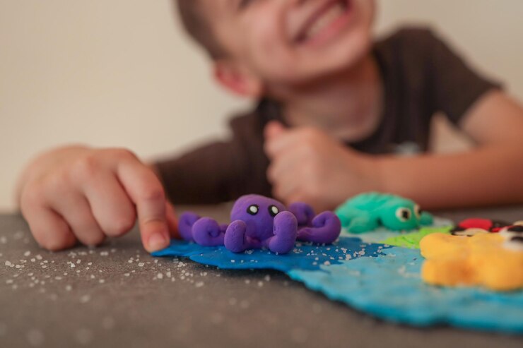 Un enfant souriant jouant avec des créatures marines colorées faites d'argile de modélisation, y compris une pieuvre violette et un crabe vert sur un fond océanique texturé