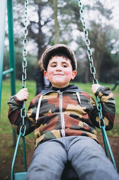 Enfant souriant jouant dans une balançoire sur une aire de jeux Profitant de loisirs au parc Vertical