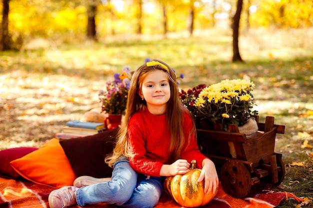 Enfant souriant avec panier de pommes rouges, assis dans un parc en automne