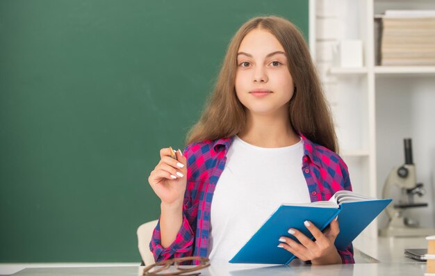 Enfant souriant prenant des notes dans un cahier de retour à l'école adolescente prête à étudier enfant faire ses devoirs avec livre adolescent étudiant éducation moderne lycée écolière avec cahier