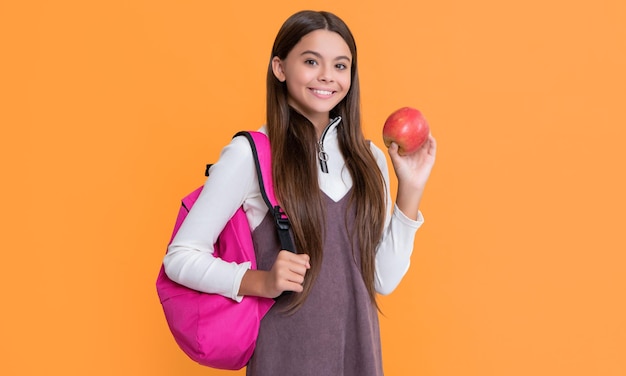 Enfant souriant avec sac à dos scolaire et pomme sur fond jaune