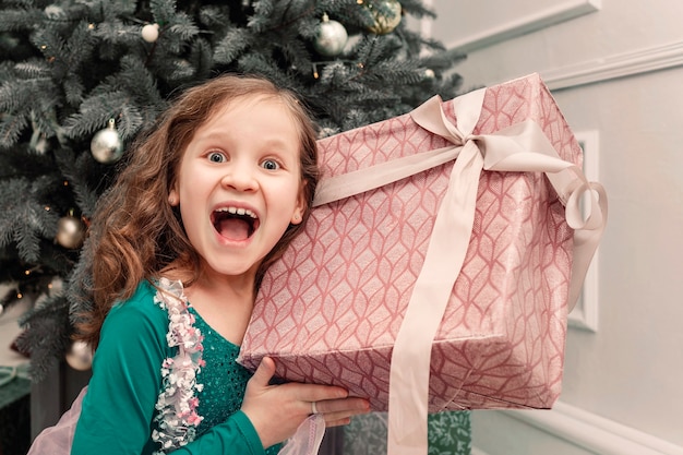 Enfant souriant tenant une boîte-cadeau du nouvel an et ouvre la bouche