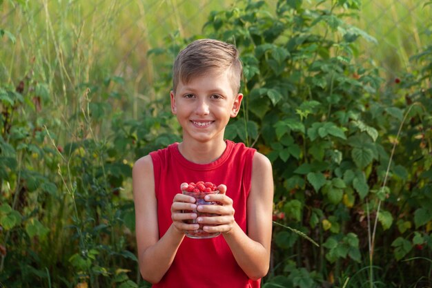 Enfant souriant tenant un pot plein de framboises fraîches prêtes à manger un jour d'été.