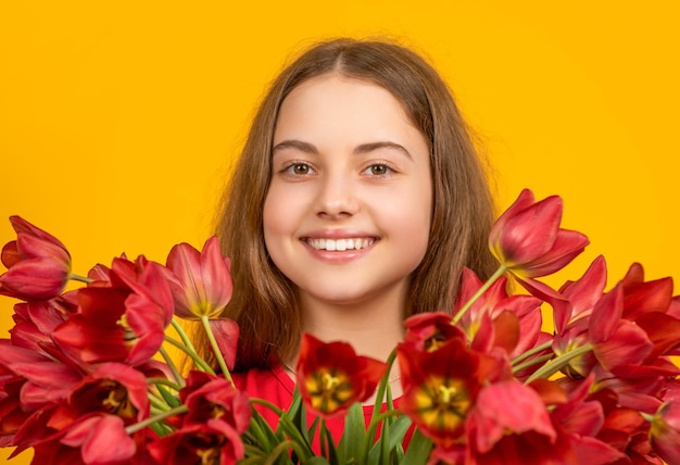 Un enfant souriant tient des fleurs de tulipes printanières sur fond jaune