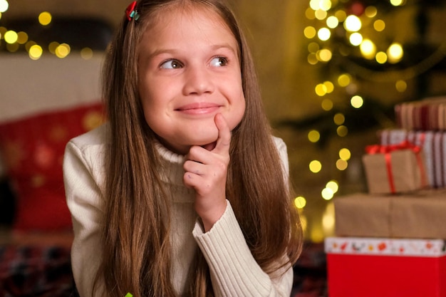 Une enfant souriante écrit une lettre au Père Noël dans la chambre, décorée pour Noël