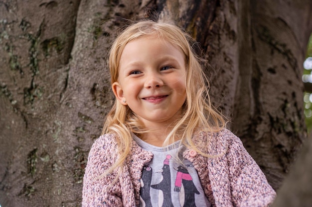 Une enfant souriante joue assise haut sur un arbre dans le parc