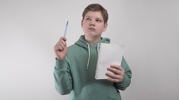 Un enfant avec un stylo et un cahier médite délibérément sur un fond blanc