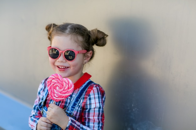 Enfant avec sucette sur un bâton dans ses mains sur le fond du mur