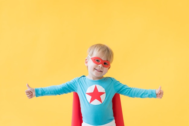 Enfant de super-héros sur fond de papier jaune. Enfant de super héros portant un masque et une cape rouges. Concept de rêve et d'imagination d'enfance